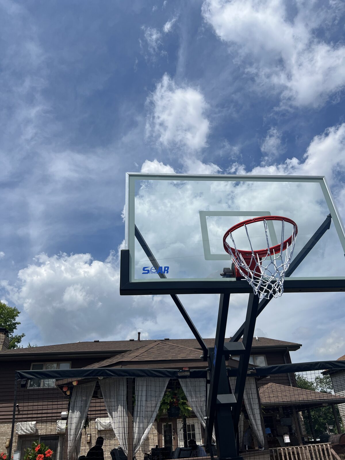 Tempered glass basketball backboard and rim viewed against the sky above a home