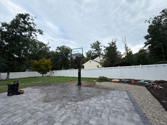 Residential paver court with a basketball hoop in a fenced backyard