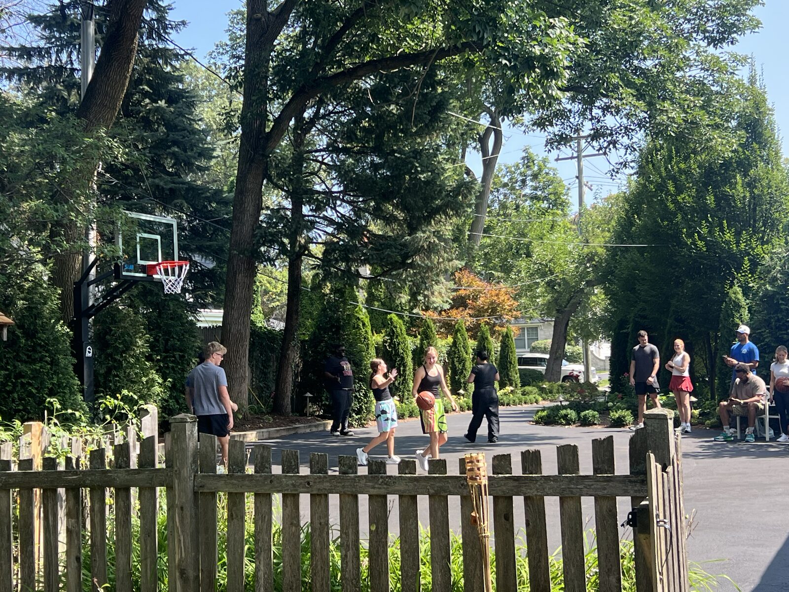 Basketball hoop installed near a fenced property line with a residential street and sidewalk beyond