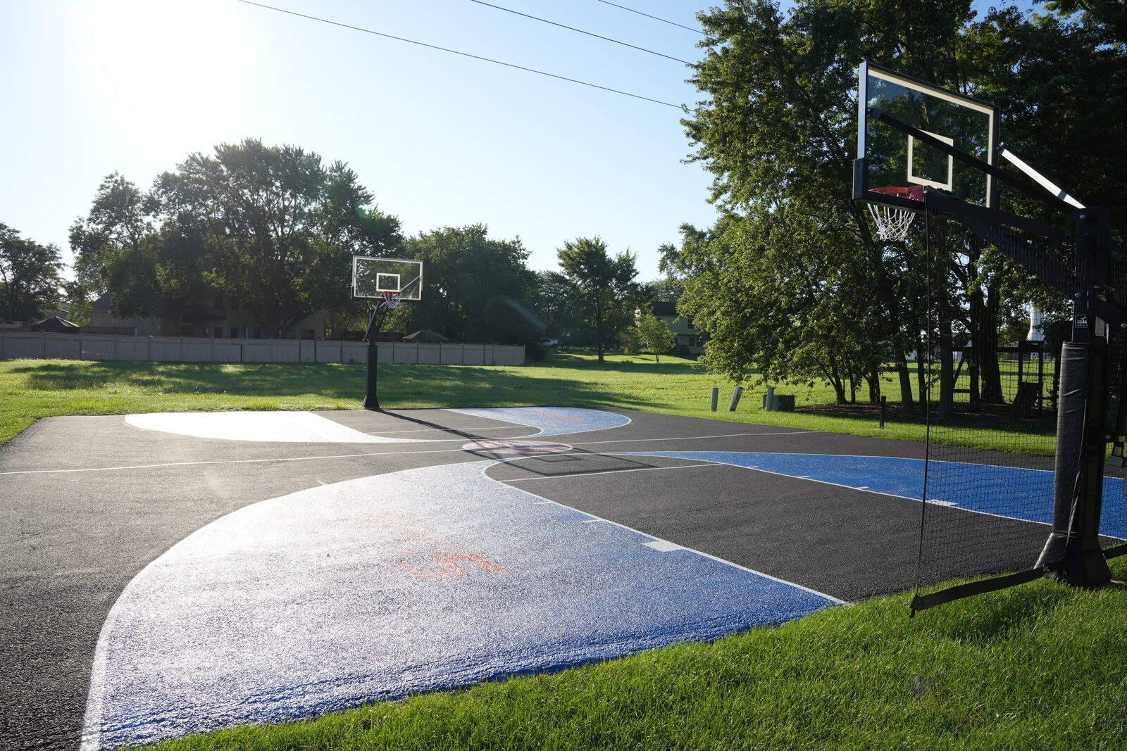 Finished residential basketball court with an in-ground hoop set at the baseline of a wide playing surface