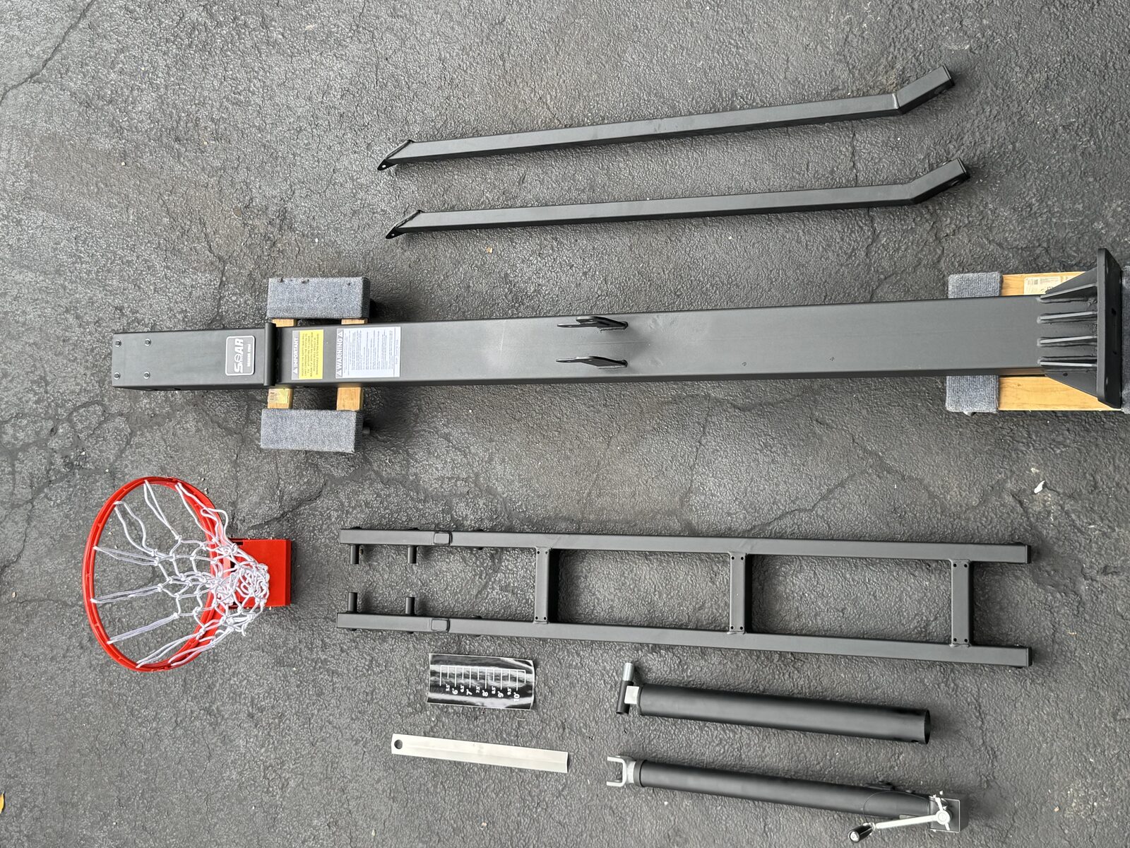 In-ground basketball system components laid out before assembly: rim, pole sections, brackets and hardware