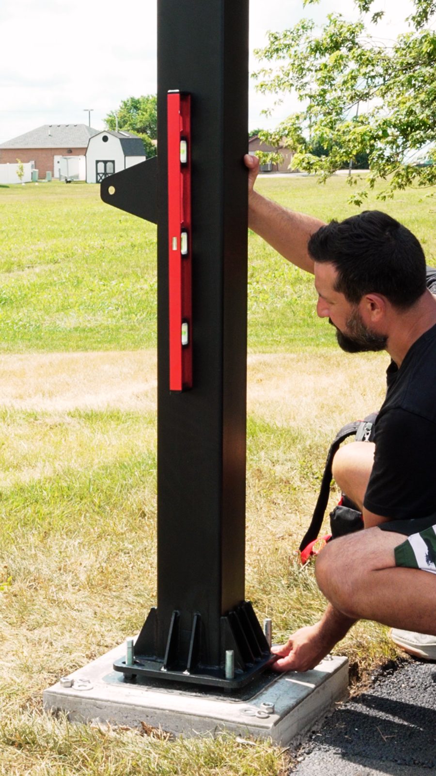 Certified installer using a level to plumb a hoop pole on its anchor plate