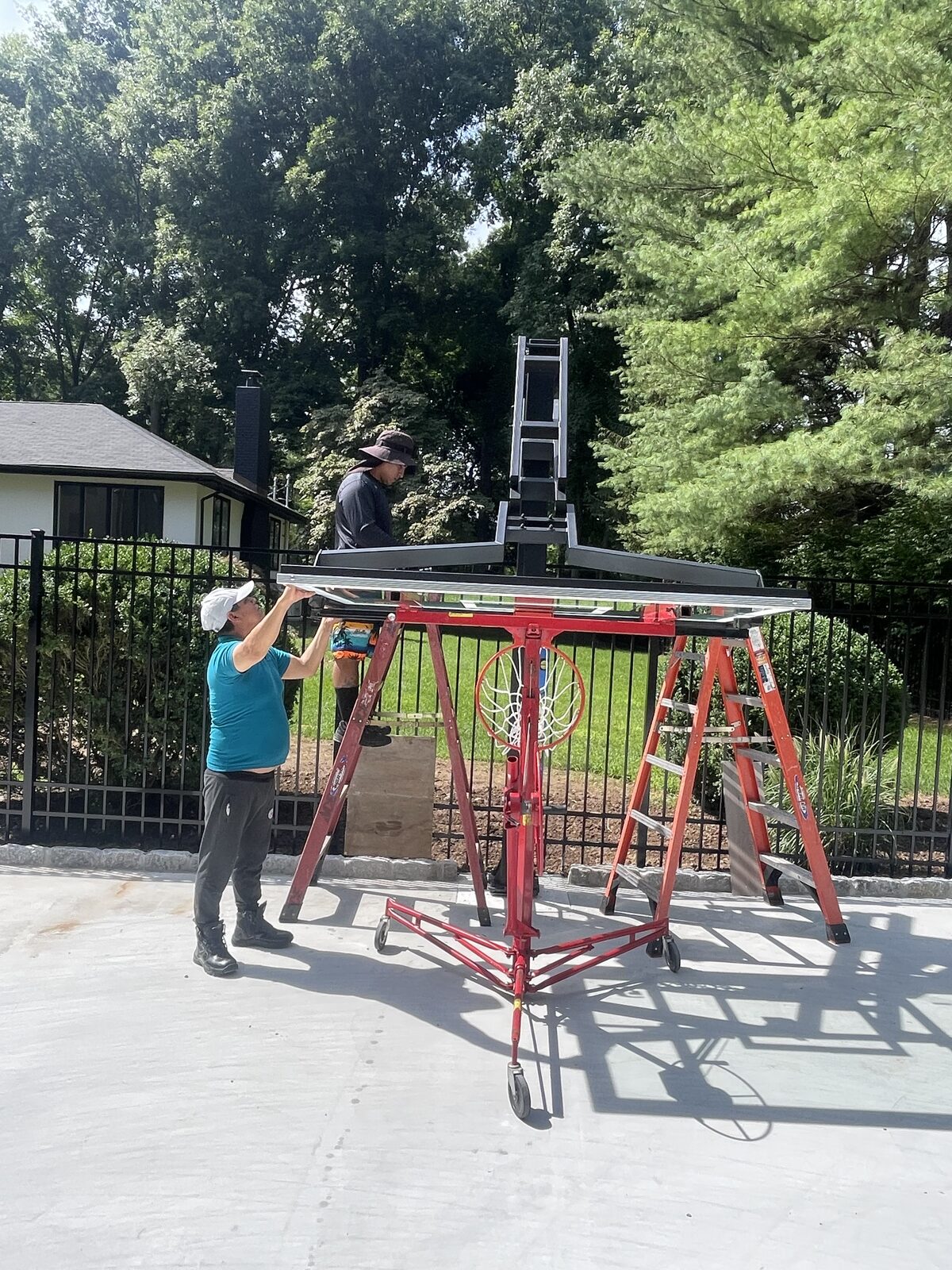 Installation crew assembling a tempered glass backboard on an in-ground basketball system