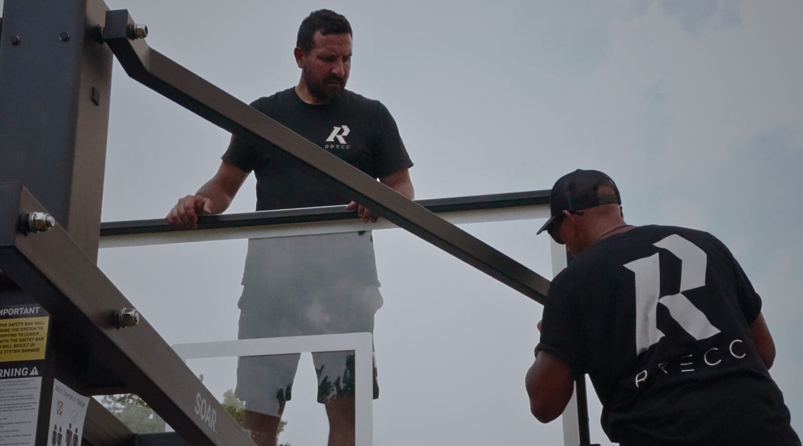 Two installers carrying the extension arm assembly of an in-ground basketball system