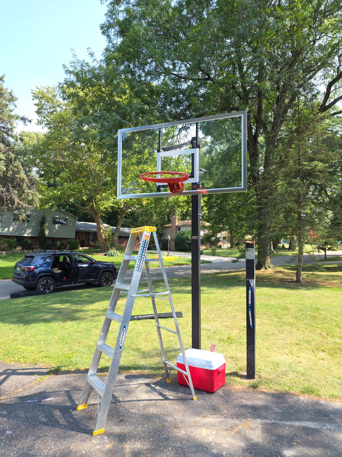 In-ground basketball hoop being installed in a front yard beside a driveway