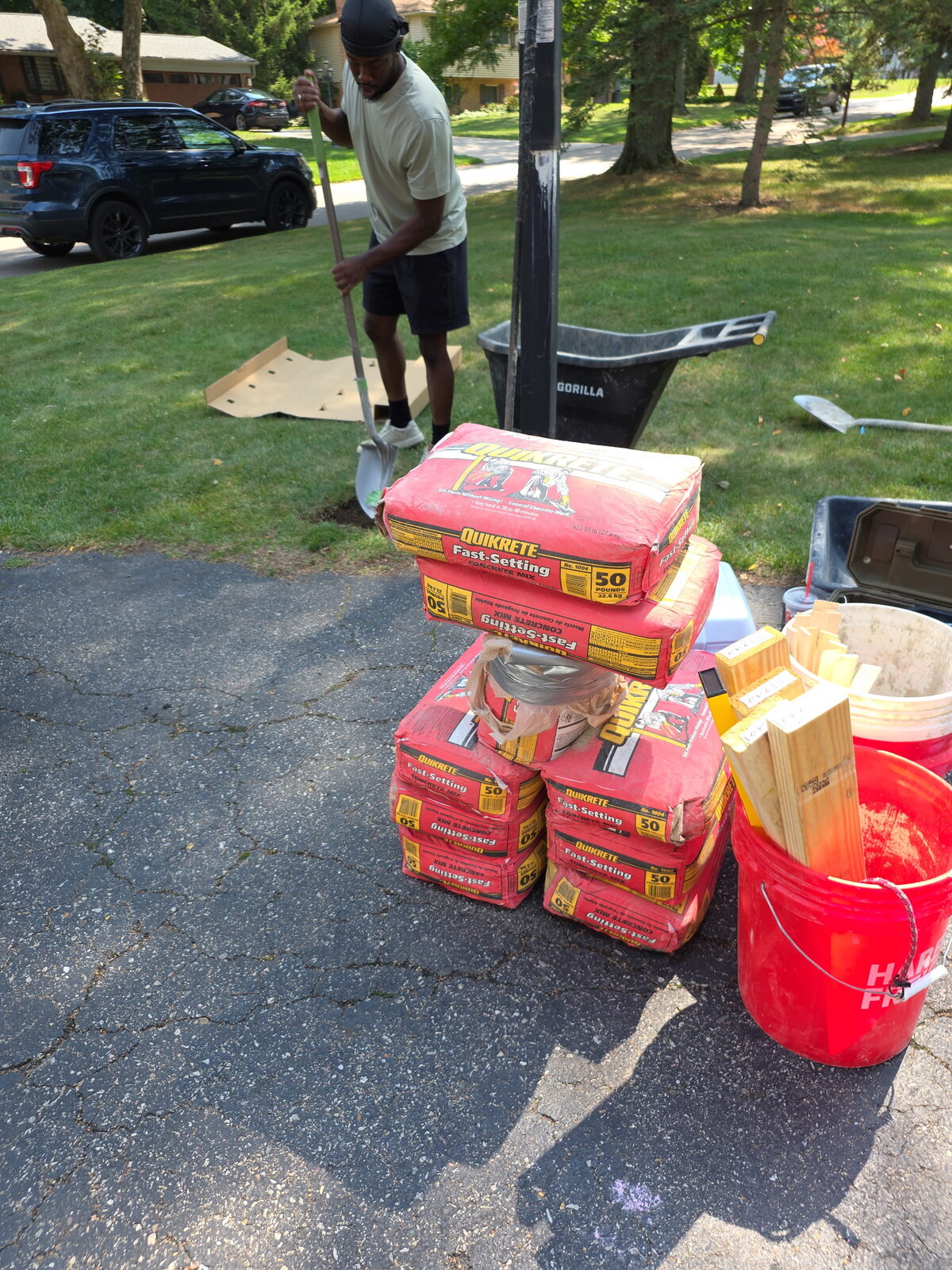 Bags of concrete mix and installation materials staged on a driveway for a hoop install