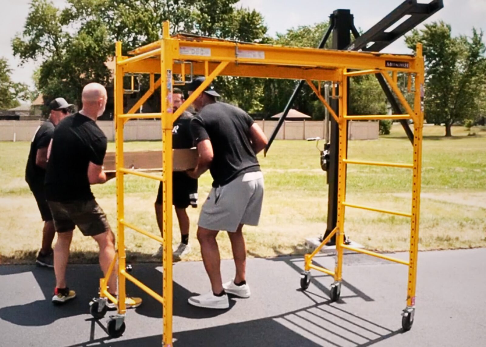Installation crew moving rolling scaffold across a residential driveway during a hoop install
