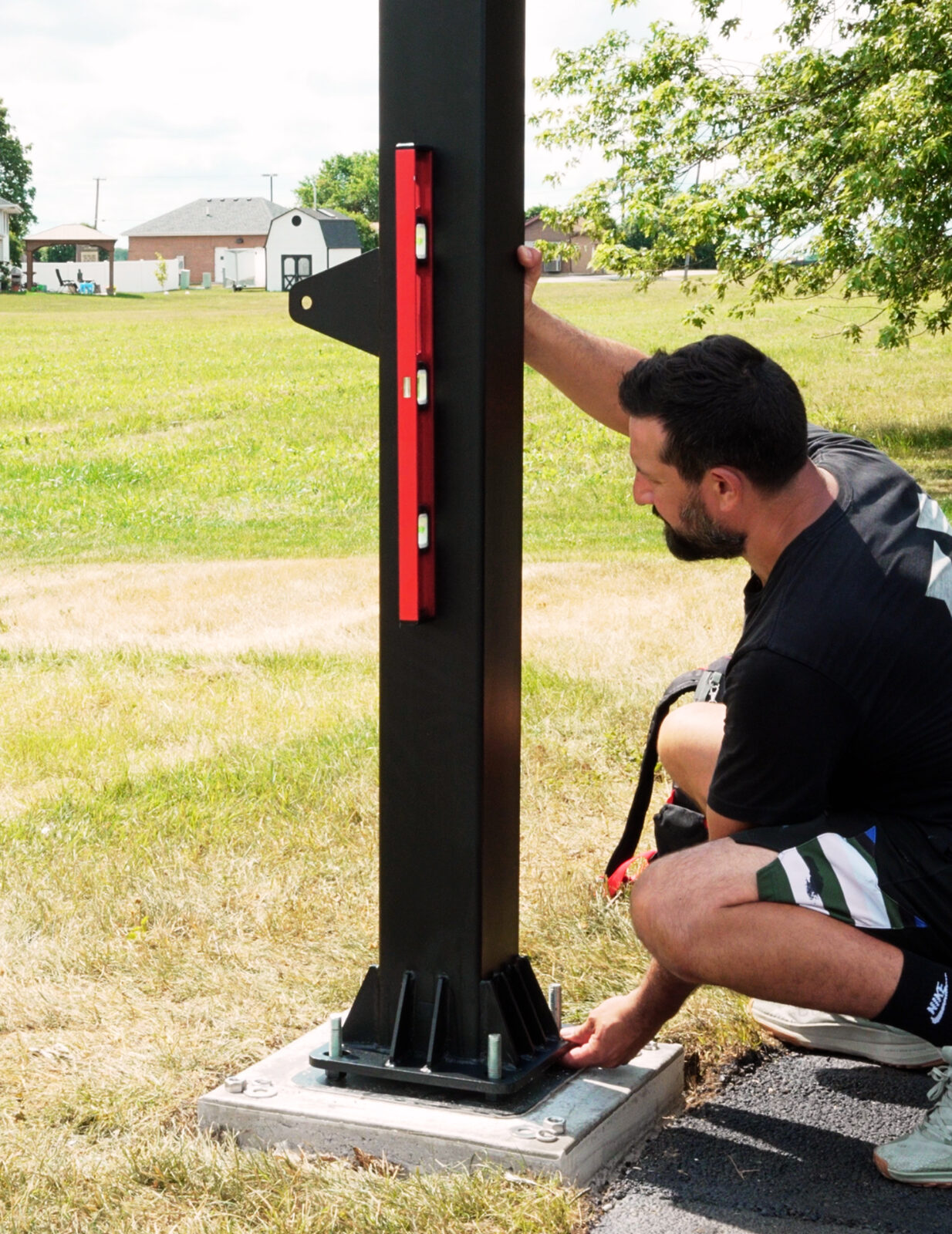 Installer setting an in-ground pole plumb on its anchor plate at the edge of a paved surface