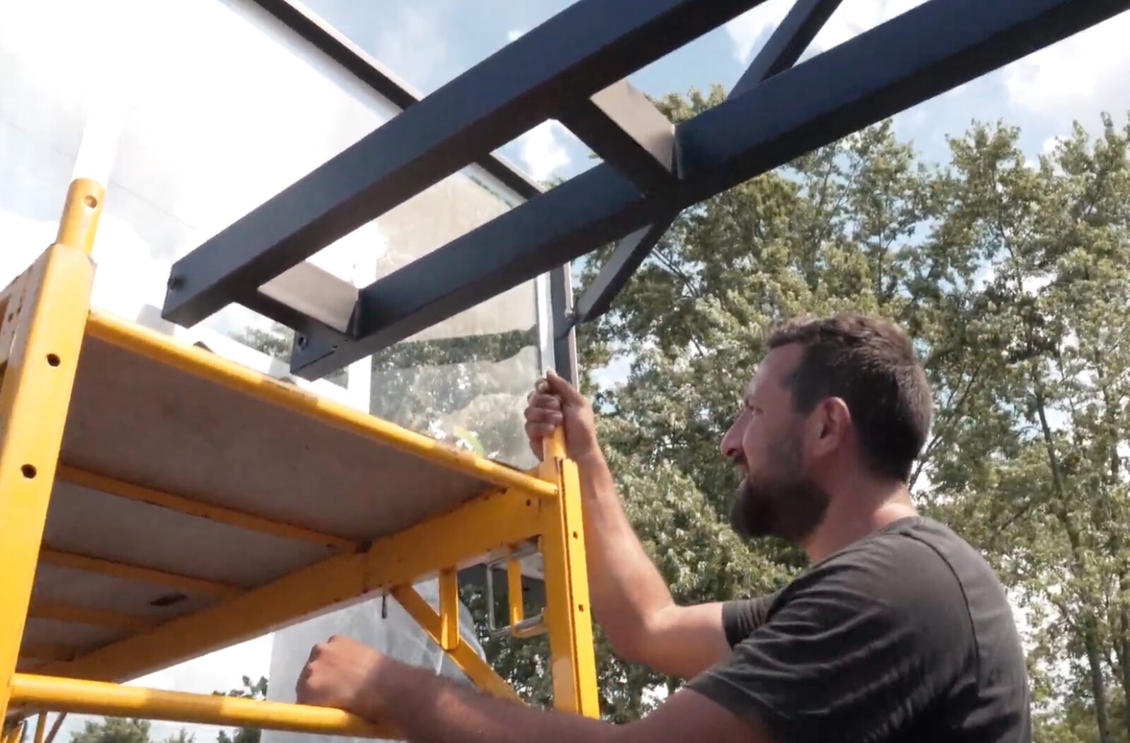 Installer supporting a basketball backboard frame during assembly on scaffolding