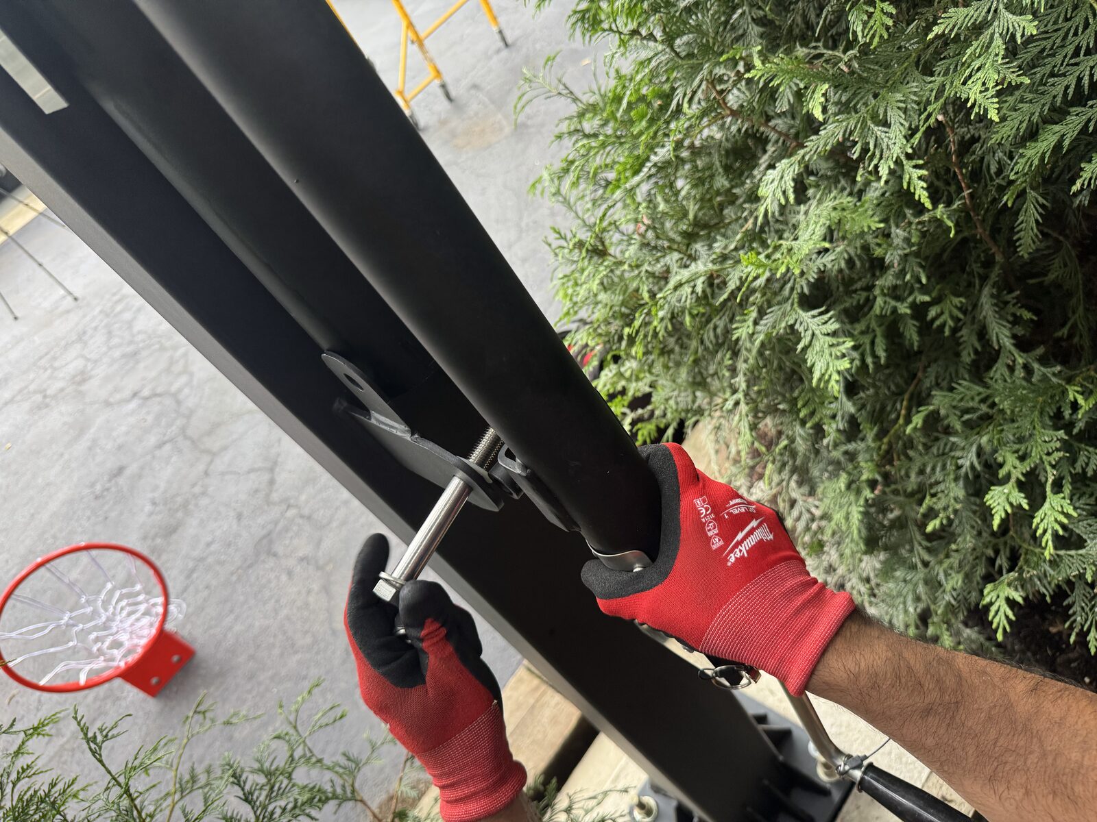 Gloved hands fitting the rim and bracket hardware to a basketball extension arm