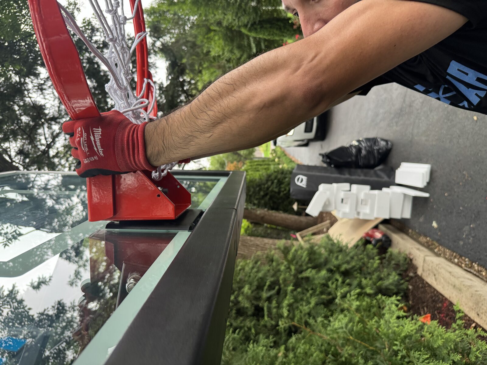 Installer's hands working on the top edge of a tempered glass basketball backboard